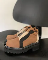 Botines marrones con suela track negra, cierre frontal con cremallera plateada y detalles en beige y negro.