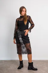 Conjunto de encaje negro, compuesto por una blusa semitransparente de manga larga con cuello alto y una falda midi recta con viso a tono.