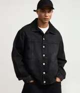 Campera masculina de jean negro con efecto desteñido, modelo boxy, con cuello solapa, manga larga con puño abotonado, cierre frontal con botones, bolsillos grandes y recortes.