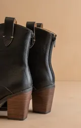 Botín negro de cuero sintético con puntera fina, caña media y tacón de madera.