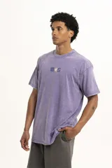 Remera color beige de corte holgado con estampado pequeño de palmera y la letra S en el centro del pecho.