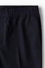 Pantalón tobillero azul marino de sarga suave con cintura elástica y cordón ajustable. Tiene bolsillos laterales y traseros ribeteados, piernas con pliegues cosidos y doblez en el bajo.