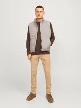Chaleco puffer gris con cuello alto y cierre frontal con cremallera. Tiene bolsillos laterales y diseño acolchado horizontal.
