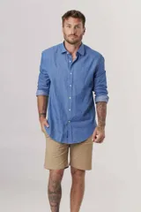 Camisa de manga larga azul denim, con cuello clásico y cierre frontal con botones. Mangas con puños abotonados y corte recto.