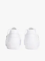 Zapatillas de corte bajo confeccionadas en piel napa color blanco. Presentan una franja lateral de tejido trenzado con los colores distintivos de la marca y una insignia metálica con el monograma TH. Cuentan con cordones al tono, suela de goma vulcanizada y logo en relieve en el talón.