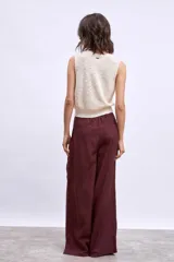 Chaleco de tejido de punto color crudo, sin mangas, con escote en V y cierre frontal de botones marrones.