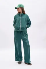 Pantalón deportivo ancho de color verde oscuro, con vivo blanco vertical en el centro de cada pierna. Presenta cordón de ajuste en la cintura y corte holgado.