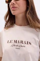 Remera color crudo de manga corta con cuello redondo y estampa marrón con la frase "Le Marais, Rue des Rosiers, France".