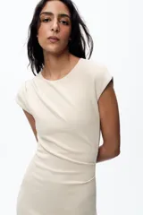 Vestido midi color beige confeccionado en hilatura con algodón. Tiene cuello redondo, manga corta caída y detalle de drapeado lateral.