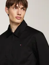 Campera negra Tommy Hilfiger de corte regular, confeccionada en puro algodón, con cuello inglés, cierre de cremallera, dos bolsillos diagonales en la cintura, un bolsillo interior abierto, puños con botón, forro completo y logo de Tommy Hilfiger bordado en el pecho.