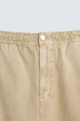 Pantalón de algodón color beige con efecto lavado, corte relajado y pierna ancha. Presenta cintura elástica con ajuste de cordón y cierre frontal con botón, además de bolsillos delanteros y bolsillos traseros de plastrón.