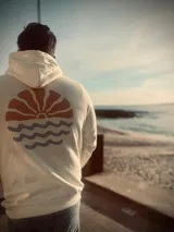 Hoodie color crema con estampado en la espalda de un sol naciente sobre el mar.