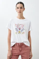 Remera blanca de algodón con cuello redondo y mangas cortas. Estampado rectangular con diseño floral y geométrico en tonos rojos, azules y amarillos.