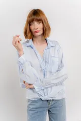 Camisa celeste de algodón con cuello camisero, botones y detalles de encaje en el escote.