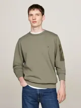 Buzo verde militar de Tommy Hilfiger, de corte clásico con cuello redondo y mangas largas. Presenta un pequeño logo bordado en el pecho y un bolsillo con cremallera en la manga izquierda.