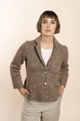 Chaqueta color crema de corte recto con cuello, solapa y bolsillos ojal. Forro solo en las mangas y terminaciones envivadas. Esquinas redondeadas y mangas con corte en puño que permiten transformarla en manga 3/4. Más larga en la espalda que en la delantera. Abrochadura con dos botones.