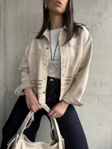 Sobrecamisa color beige de gamuza sintética con cuello camisero, cierre frontal con botones dorados, bolsillos de parche en el pecho y bajo con calados.