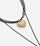 Collar de varias capas compuesto por finos cordones negros y un dije central en forma de corazón con superficie texturizada. Presenta un acabado en oro envejecido y cierre ajustable.