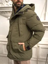 Campera verde militar con capucha, cierre frontal con cremallera y broches, bolsillos laterales con solapa y puños ajustables con velcro.