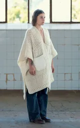 Ruana abierta color crudo, tejida a mano en crochet con lana merino uruguaya. Presenta textura combinada de puntos y trenzas, y bolsillos de cuero vacuno aplicados manualmente.