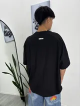 Remera negra de manga corta con cuello redondo y detalles en blanco en los hombros. Presenta un estampado con el logo de la marca en el frente.