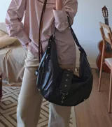Cartera tipo hobo de cuero negro con correa de hombro ajustable y detalles de tachas en forma de estrella.