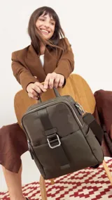 Mochila negra combinada, con cuerpo principal de tela impermeable y bolsillo frontal de simil cuero texturizado. Cuenta con asa corta superior y correa larga ajustable para llevar al hombro o cruzada.