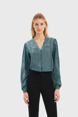 Camisa verde azulado con escote en V, mangas largas abullonadas y cierre frontal con botones.