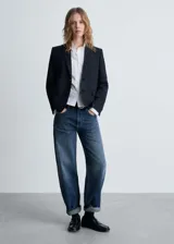 Blazer negro con raya diplomática, cuello con solapa, cierre con botones, manga larga con puños abotonados, diseño recto y estructurado, bolsillo de ribete en el pecho y dos bolsillos de ribete con solapa laterales.