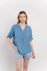 Camisa celeste de lino con escote en V abotonado, bolsillo frontal y mangas cortas con trabilla.