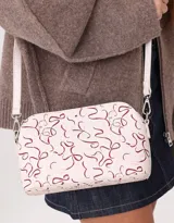 Bandolera negra de cuerina con doble compartimento con cierre y charm lateral. Tiene correa regulable y desmontable.