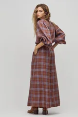 Camisa larga de lino a cuadros color avellana, con cuello camisero clásico, mangas largas abullonadas con puños elásticos, botones de nácar frontales y ruedo curvo, un poco más largo atrás. Incluye cinturón de cuero marrón.