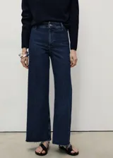 Pantalón de jean azul oscuro, de corte ancho, tiro alto y largo cropped. Presenta cierre de cremallera y botón, trabillas para cinturón, bolsillos traseros y bajo deshilachado.