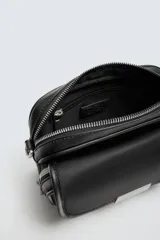 Bandolera negra de nylon con correa ajustable y removible. Tiene un compartimento principal con cierre de cremallera, un bolsillo interior plano con cremallera y un bolsillo frontal con solapa y cremallera.
