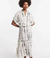 Vestido midi de viscosa color blanco con estampado de bloques negros, corte evasé, mangas cortas, cuello camisero, lazo en la cintura y cierre frontal con botones.