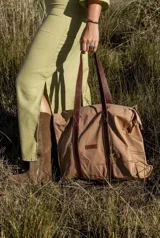 Bolso tote color beige con asas de cuero marrón, cierre superior y bolsillo interno.