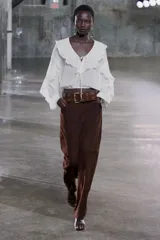 Blusa color marrón con escote en pico, manga larga abullonada con elástico en los puños y volantes en el escote y mangas.