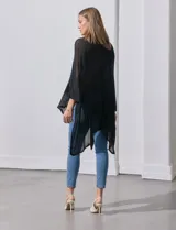 Poncho negro de tejido calado con lurex, terminación asimétrica y cuello redondo.