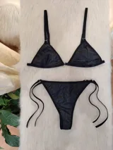 Conjunto de bikini negro con destellos verticales multicolor. El corpiño es de corte triangular con breteles finos regulables y aro metálico en el centro. La bombacha es tipo colaless con tiras laterales regulables.