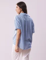 Blusa celeste y blanca a rayas verticales, con cuello con solapa y escote en V. Delantera cruzada con abertura simulada y mangas cortas.
