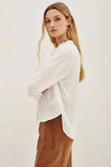 Camisa blanca de manga larga con cuello mao y escote en V, con bordados negros en el frente y puños.