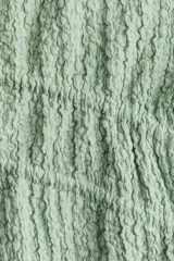 Top corto verde agua en punto arrugado con escote en V y doble cordón de ajuste abajo del busto que se enlaza adelante. Mangas cortas con elástico revestido y ribete sobrehilado.