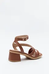 Sandalia de cuero color marrón, con tiras cruzadas y pulsera al tobillo con hebilla metálica. Taco ancho medio.