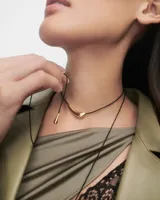 Gargantilla con cordón negro y dije dorado en forma de lágrima.