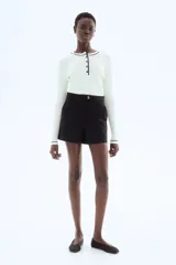 Short negro de tiro alto con cierre y pretina prolongada con botón. Modelo con bolsillos al bies y bolsillos insertados decorativos atrás.