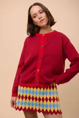 Cárdigan negro de punto con cuello redondo, cierre frontal con botones celestes y ribetes en cuello y puños de color rojo.