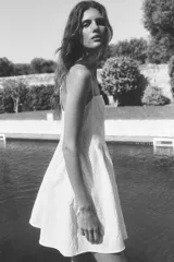 Vestido corto blanco en tejido jacquard con escote recto y breteles spaghetti ajustables. Modelo con cuerpo entallado, pliegues en la cintura y pollera con vuelo. Cierre oculto y cierre de corchete en la espalda. Parcialmente forrado.