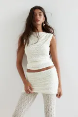 Pantalón largo de encaje blanco con corte acampanado y falda mini superpuesta con laterales fruncidos y cintura elástica.