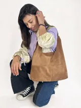 Bolso tipo hobo de gamuza color marrón, con asa de hombro y parche con logo de la marca en el frente.