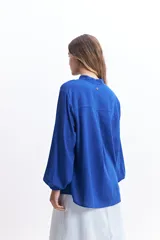 Camisa azul de manga larga con cuello mao, corte holgado y cierre frontal con botones.